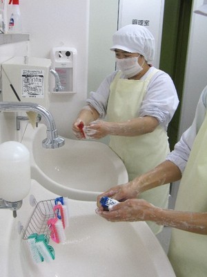 調理員さんが、石けんとブラシを使って手を洗っている写真