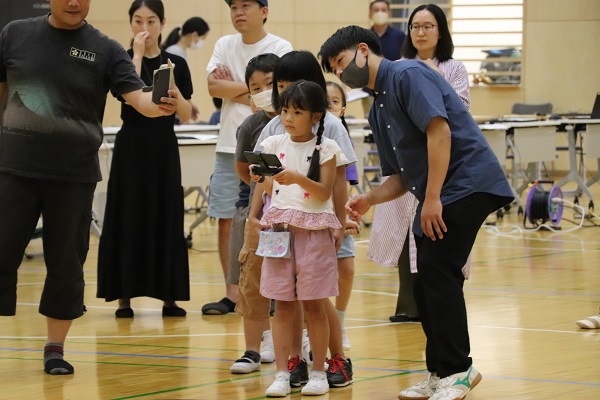 ドローンを飛ばす女の子とサポートする大学生